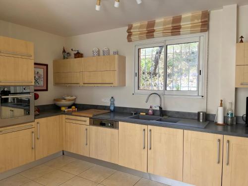 une cuisine avec des armoires en bois, un évier et une fenêtre dans l'établissement Charmante villa avec spa et panorama, à Lorgues