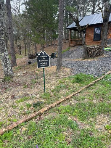 a sign in the grass next to a log cabin at The Knotty Pine Cabin at Cabins of Wolf Pen Gap in Mena