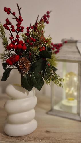 a white vase with red berries and christmas decorations at Adriano Park View in Crescenzago