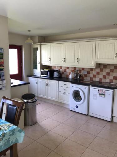 a kitchen with white cabinets and a washer and dryer at Sunny Beaches in Ballinskelligs