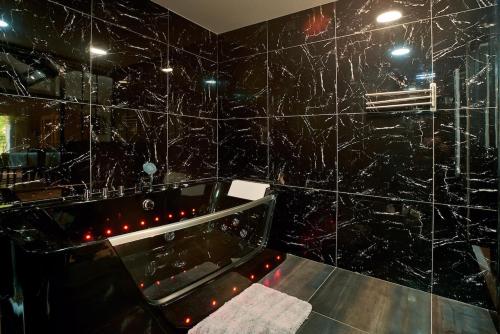 a black tiled bathroom with a tub and a mirror at Versailles One Sauna & Jacuzzi in Versailles
