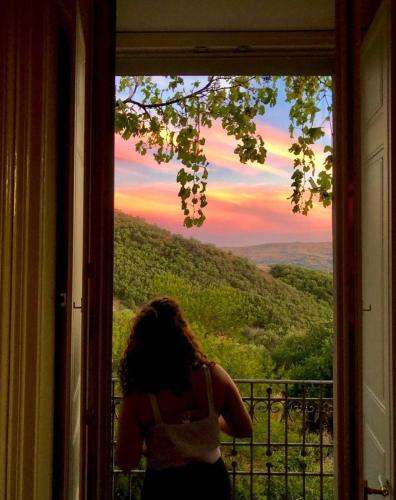 a woman looking out a window at a sunset at Villa Pietralunga in the woods in Nicosia