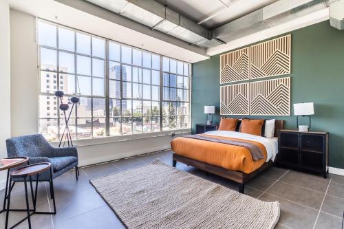 a bedroom with a bed and a chair and windows at DTLA 2BR Rooftop Jacuzzi & Sunset Views in Los Angeles