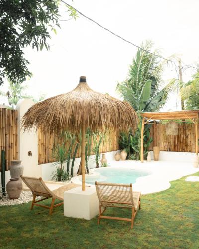 a pool with two chairs and a straw umbrella at Tyde Bali Boutique Hotel in Uluwatu