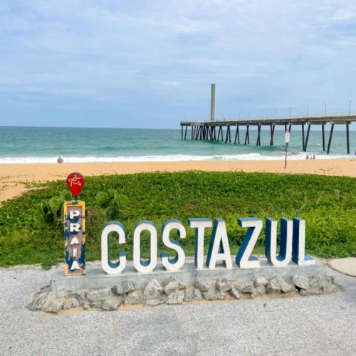 a sign for a beach with a pier in the background at Pousada Recanto dos Charri in Rio das Ostras