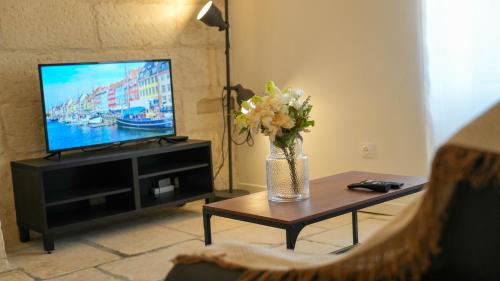 a living room with a television and a vase of flowers on a table at NEW! Wifi, Netflix Le Refuge des Berges in Beaucaire