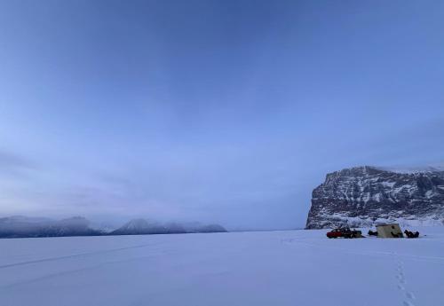 a snow covered field with a mountain in the background at Ice Hut on the Sea Ice in Uummannaq