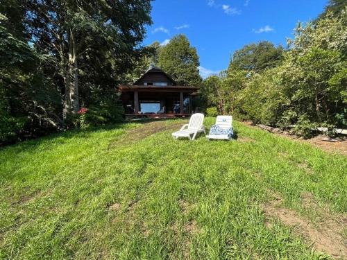 two white chairs sitting in the grass near a gazebo at Casa a orilla de Lago Panguipulli in Panguipulli