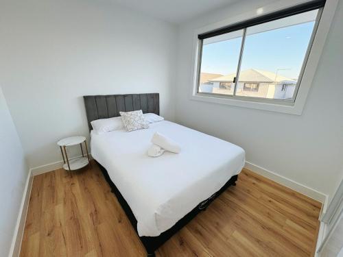 ein Schlafzimmer mit einem weißen Bett mit einem Fenster in der Unterkunft Brand New Luxury 4 Bedroom House in Marsden Park