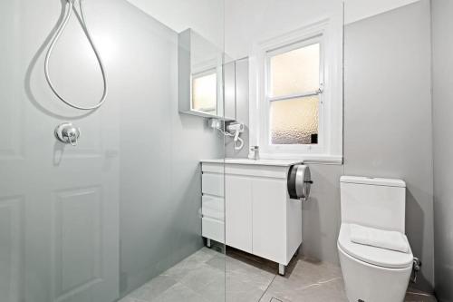 a white bathroom with a toilet and a window at Quaint Double Room - Seconds to Shops & Eateries - Shared Bathroom in Sydney