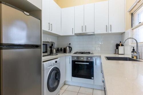 a kitchen with white cabinets and a washer and dryer at Peaceful and Stylish Petersham Aparttment with Parking in Sydney