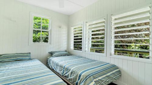 two beds in a room with white walls and windows at Moomba On Main in Wooli