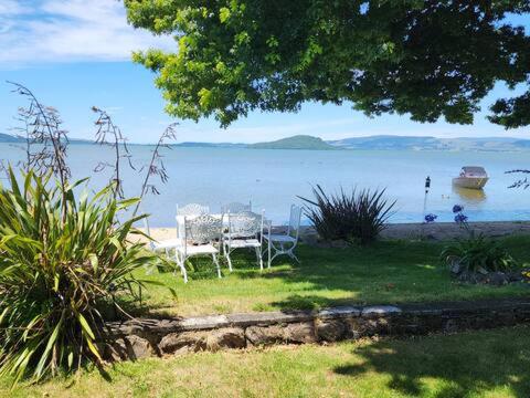a table and chairs sitting on the grass near the water at Lake view room with bathroom in Rotorua