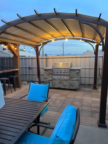 a patio with a grill and blue chairs under a pergola at NEW Pool Spa Firepit Pool Table Sleeps 12 in Lake Havasu City