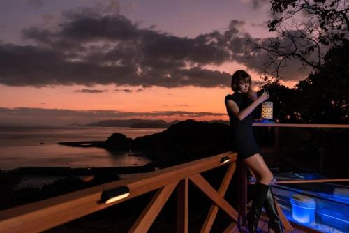 a woman standing on top of a fence with the sunset at Viva Sumoto in Amakusa