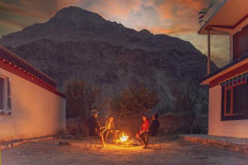 a group of people sitting around a fire in front of a mountain at Echor Mud Huts Tabo, Spiti Valley in Kaza