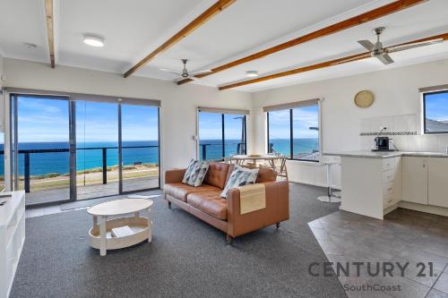 a living room with a couch and a kitchen with windows at See-Sea House - Sellicks Beach - C21 SouthCoast Holidays in Sellicks Beach