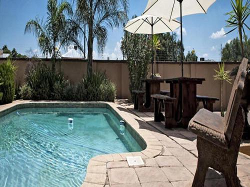 a pool with a chair and a table and an umbrella at La Casa Mia Guesthouse in Kimberley