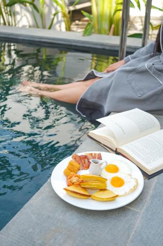 a plate of eggs and fruit and a book next to a pool at veHaa BOUTIQUE HOTEL in Phnom Penh