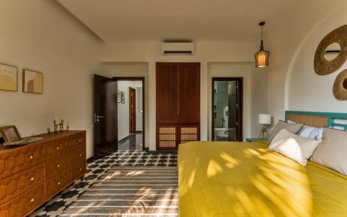 a bedroom with a yellow bed and a bathroom at La Masillia, 2 BHK with Private Pool, 15 mins from Morjim Beach, Wifi, Peaceful location, Kitchen, Security, Patio in Siolim