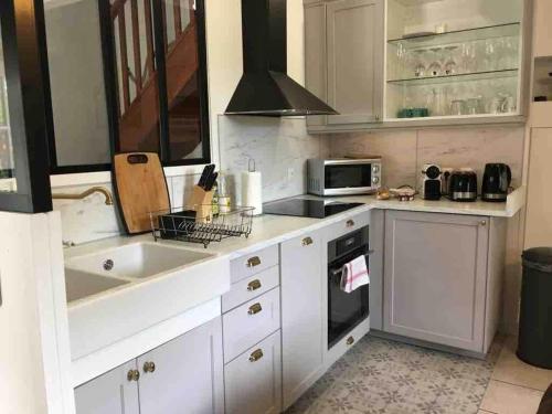 a kitchen with white cabinets and a sink and a microwave at Gîte La Maisonnette à Auvers-sur-Oise in Auvers-sur-Oise