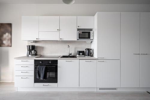 a white kitchen with white cabinets and a microwave at Vesirattaantie Apartment in Espoo