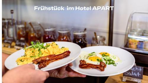 a person holding two white plates with food on them at BRIX - Self Check-In Hotel in Rotkreuz