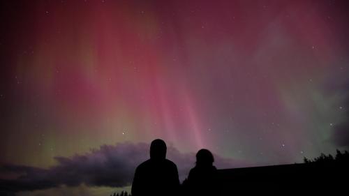 two people sitting on a hill watching the northern lights at Fiordland Eco-Retreat -- Panoramic Views -- Hot Tub in Te Anau