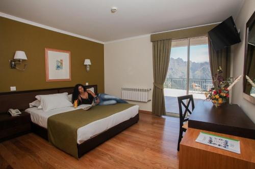 une femme allongée sur un lit dans une chambre d'hôtel dans l'établissement Eira do Serrado - Hotel & Spa, à Curral das Freiras