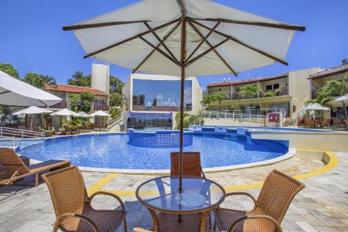 a table with an umbrella in front of a swimming pool at TRIPLEX Solar Água- by Pipa Praia House in Pipa