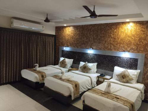 a hotel room with three beds and a ceiling fan at Hotel Mayas in Tiruchchirāppalli
