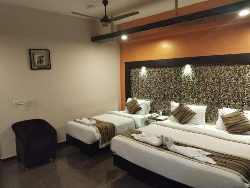 a hotel room with two beds and a chair at Hotel Mayas in Tiruchchirāppalli