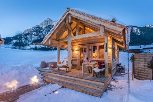a wooden cabin in the snow with a table and chairs at Chalet Grand Flüh - Alpiner Luxus & Spa in Nesselwängle