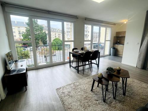 - un salon avec une table, des chaises et de grandes fenêtres dans l'établissement Abaca YourHostHelper, à Caen