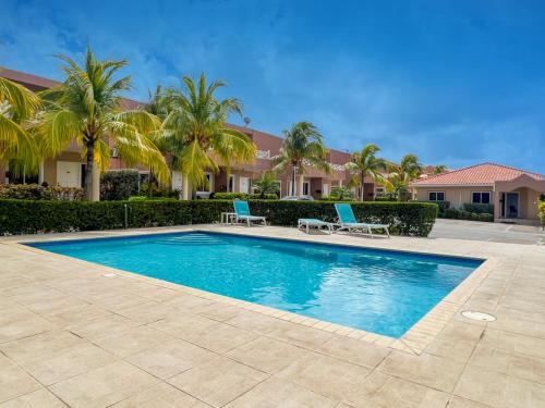 a swimming pool with two blue chairs and palm trees at Caribbean Beach Resort 3, Piscadera - Casa D'Oro in Sint Michiel