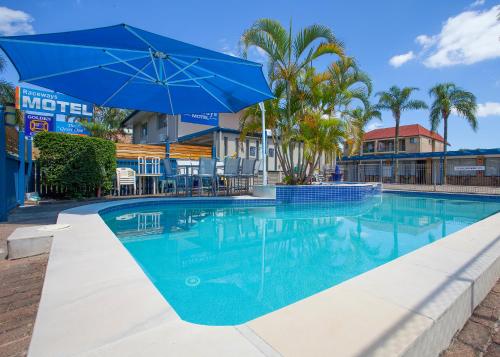 a swimming pool with a blue umbrella and palm trees at Raceways Motel in Brisbane