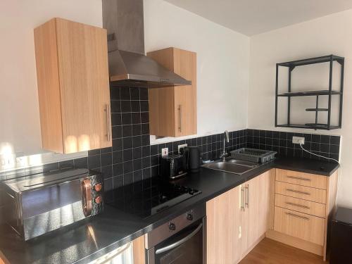 a kitchen with black tiled walls and wooden cabinets at Top floor 2 bedroom retreat in Morley