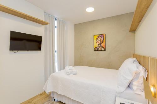a bedroom with a white bed and a television at Elysia in Curitiba