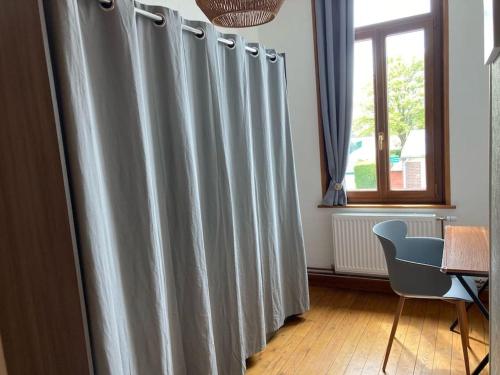 Cette chambre dispose de rideaux gris, d'une table et d'une chaise. dans l'établissement Le refuge cosy Amiens, à Saleux