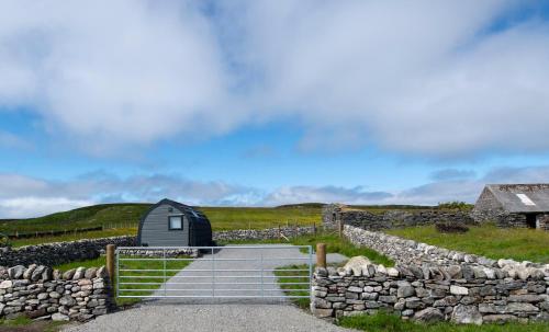 a small house in a field next to a stone wall at 21 Callanish Luxury Pod in Callernish