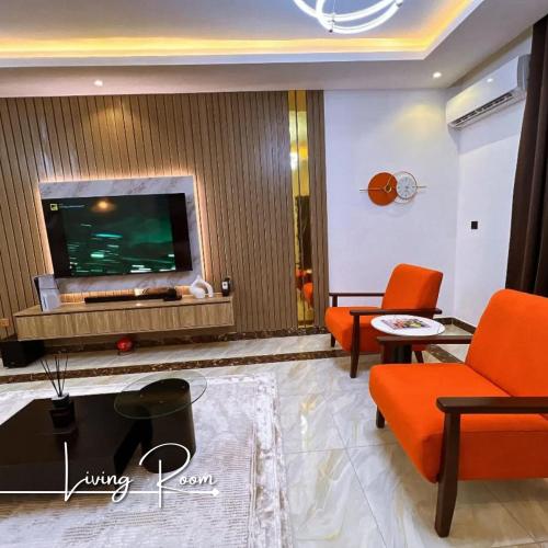 a living room with orange chairs and a flat screen tv at Desireé by StayHub - Luxury 3 Bedroom with PS5 in Jahi in Abuja