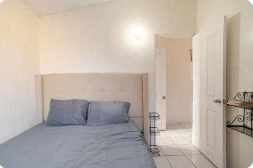 a bed with blue pillows in a white bedroom at Mi Casita bonita, libre de humo, pet friendly in Ensenada