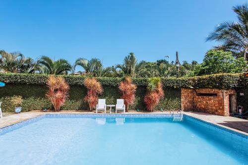 a swimming pool with two chairs and a hedge at VELINN Pousada Casa de Pedra Ilhabela in Ilhabela
