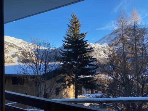 un arbre devant un bâtiment avec des montagnes enneigées dans l'établissement Studio LE DAHUT, à Orcières