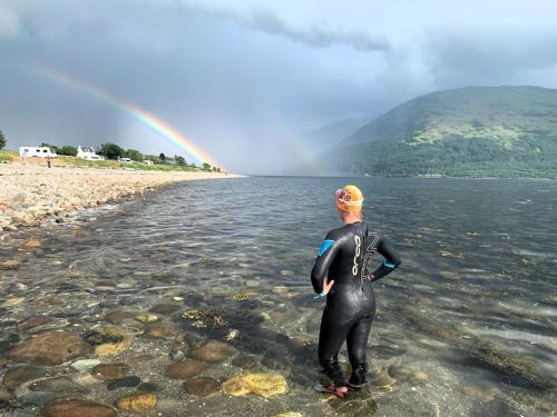 a man standing in the water with a rainbow in the background at Sandpiper Caravan in Onich