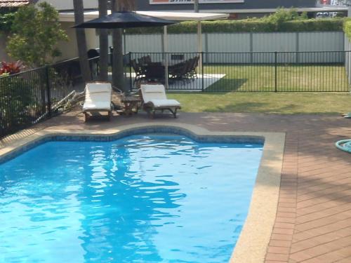 a swimming pool with two chairs and an umbrella at Caravilla Motor Inn in Taree