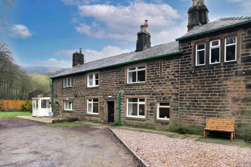 an old brick house with a bench in front of it at Dovestone Cottage in Oldham
