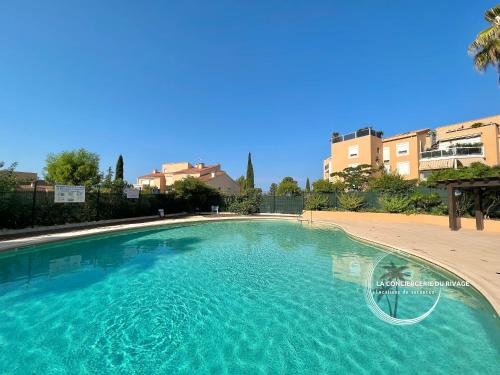 une grande piscine à l'eau bleue devant quelques bâtiments dans l'établissement La Frégate - Grand Appartement avec vue sur la mer - Piscine, à Carqueiranne