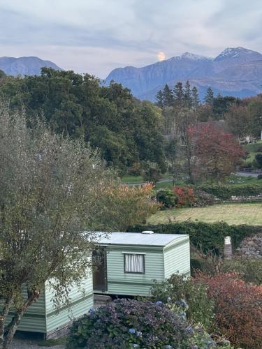 a tiny house in a garden with mountains in the background at Sandpiper Caravan in Onich