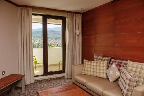 a living room with a couch and a large window at Ruskovets Thermal SPA & Ski Resort in Bansko